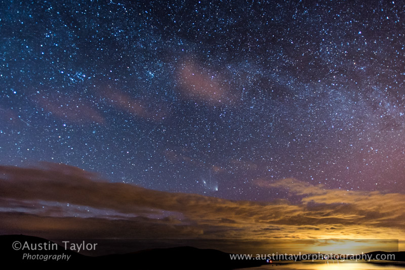 Comet C/2011 L4 (PANSTARRS) with Andromeda Galaxy (M31) and a satellite flying between the pair over Stream Sound, the lights from Scalloway in the distance.